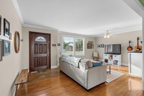 Ein Wohnzimmer mit einer Couch, einem Fernseher, einer Gitarre und einer Tür mit einem Buntglasfenster.