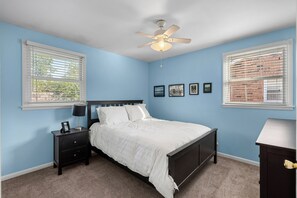 Ein Schlafzimmer mit Bett, Nachttisch, Lampe, Deckenventilator und gerahmten Bildern an der Wand.