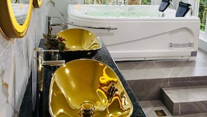 Casa de banho moderna com uma banheira grande, duas pias douradas e um espelho amplo.