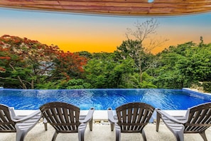 A pool with clear blue water, surrounded by greenery and trees, under a wooden pergola. - Monk Punta Fuego Beach House (Nasugbu)