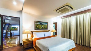 Quarto de hotel com cama, duas luminárias de cabeceira, um quadro, uma escada e uma janela com cortinas.