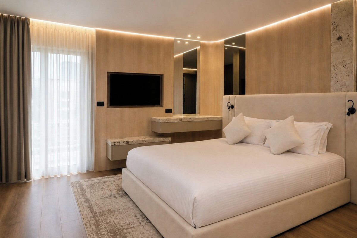 A modern bedroom with a large bed, a flat-screen TV mounted on the wall, and a built-in vanity with a mirror.
