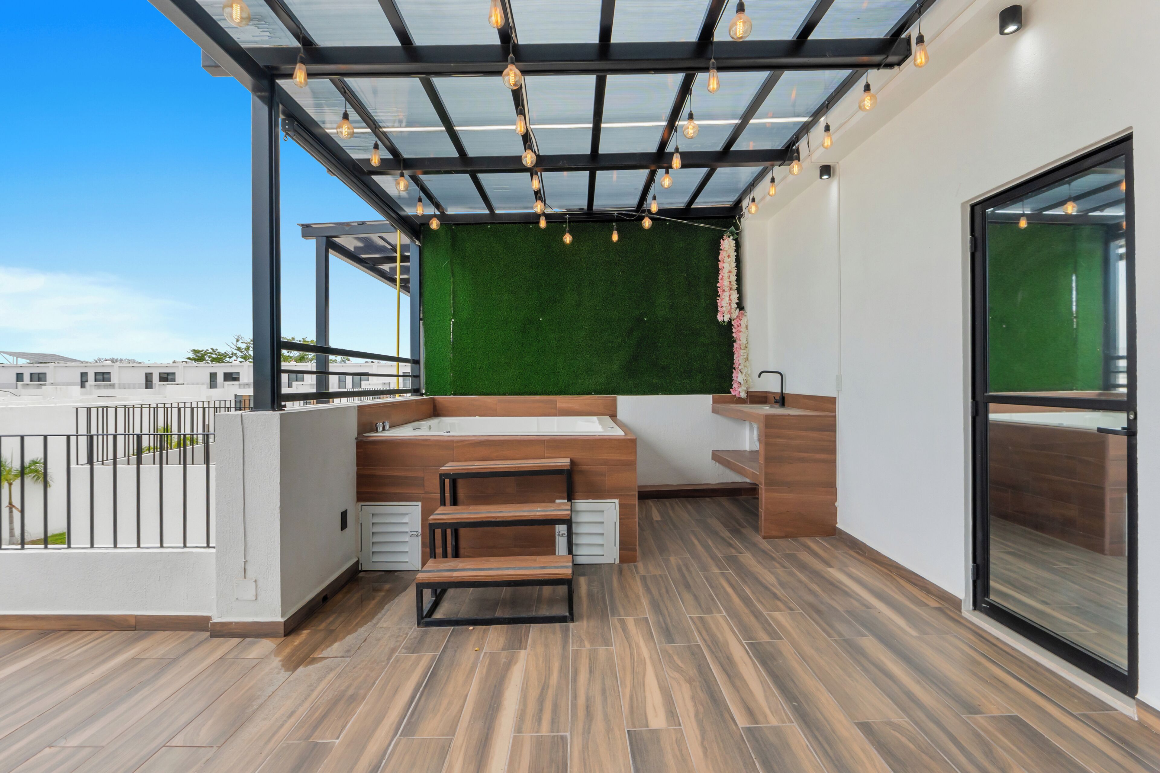 A modern outdoor balcony with a wooden floor, a built-in sink, and a green wall.