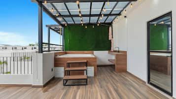 A modern outdoor balcony with a wooden floor, a built-in sink, and a green wall.