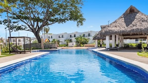 A swimming pool with a thatched-roof structure and lounge chairs on one side.