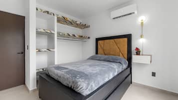 A bedroom with a bed, built-in shelving, an air conditioning unit, and a wall-mounted light fixture.