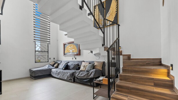 A modern living room with a grey sectional sofa, a wooden staircase, and a framed artwork on the wall.