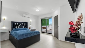 A modern bedroom with a bed, bedside lamps, a view of the outdoors, and a bathroom with a shower.