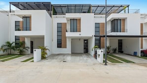 A modern multi-story residential building with a covered driveway and a carport.