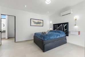 A modern bedroom with a black bed frame, a blue bedspread, and a framed artwork on the wall.