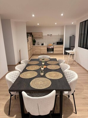 A modern dining area with a dark wooden table, white cushioned chairs, and woven placemats. - The Volcanoes Refuge (Saint-Pierre-le-Chastel)