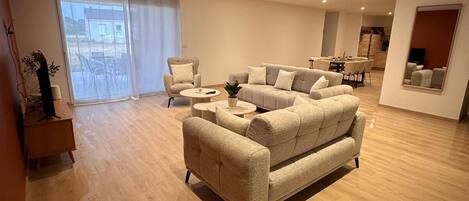 A spacious living room with a large sofa, a coffee table, and a dining area with chairs.
