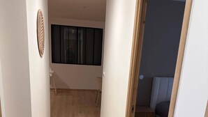 Um corredor com piso de madeira, um tapete redondo e uma porta que dá para um quarto com cama e janela.