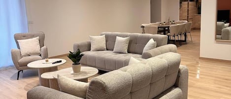 A modern living room with a sectional sofa, a small round coffee table, and a dining area in the background.