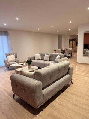 A modern living room with a sectional sofa, a small round coffee table, and a dining area in the background. - The Volcanoes Refuge (Saint-Pierre-le-Chastel)