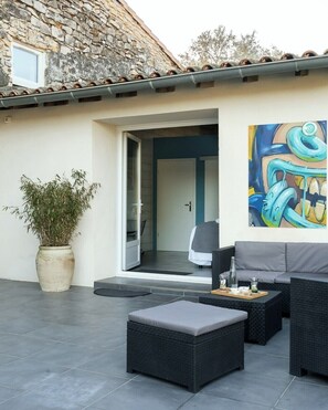 A modern outdoor living area with a stone wall, a large potted plant, and a dining table with outdoor seating. - Vrbo Property (Nîmes)