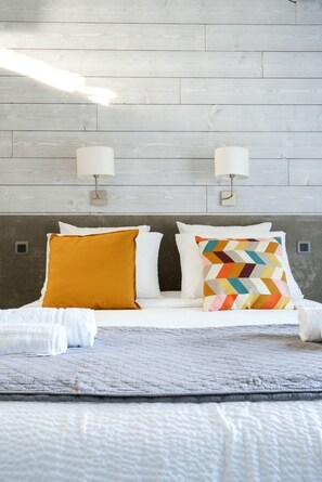 A bed with white bedding, two wall-mounted lamps, and a wooden headboard. - Vrbo Property (Nîmes)