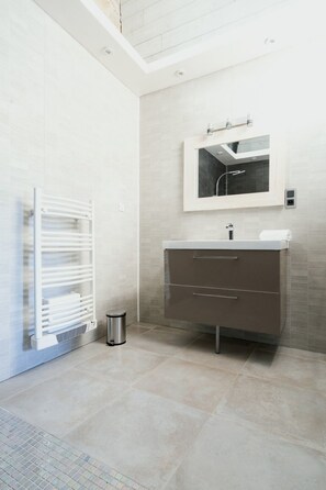 A modern bathroom with a white vanity, a mirror, and a towel rack. - Vrbo Property (Nîmes)