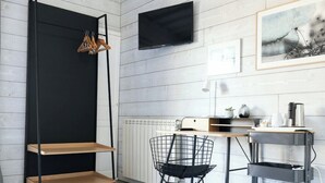 Een moderne kamer met een zwarte plankenwand, een zwarte stoel, een bureau met een computer, een aan de muur bevestigde televisie en een ingelijst beeld.