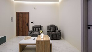 A room with two grey massage chairs, a wooden table with a vase and a remote control, and a wooden door. - 2BR Serviced Apartment in Al Rimal  Near PNU & Riyadh Airport (الرياض)