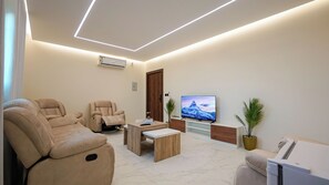 A modern living room with a flat-screen TV, two reclining chairs, a coffee table, and a small side table. - 2BR Serviced Apartment in Al Rimal  Near PNU & Riyadh Airport (الرياض)