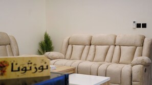 A beige sofa in a room with a small table and a potted plant. - 2BR Serviced Apartment in Al Rimal  Near PNU & Riyadh Airport (الرياض)
