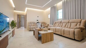 Ein modernes Wohnzimmer mit einer Couch, Sesseln, einem Couchtisch, einem Fernseher und einer Pflanze.