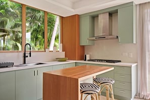 Una cocina moderna con una isla de madera, armarios verdes y un ventanal con vistas a palmeras.