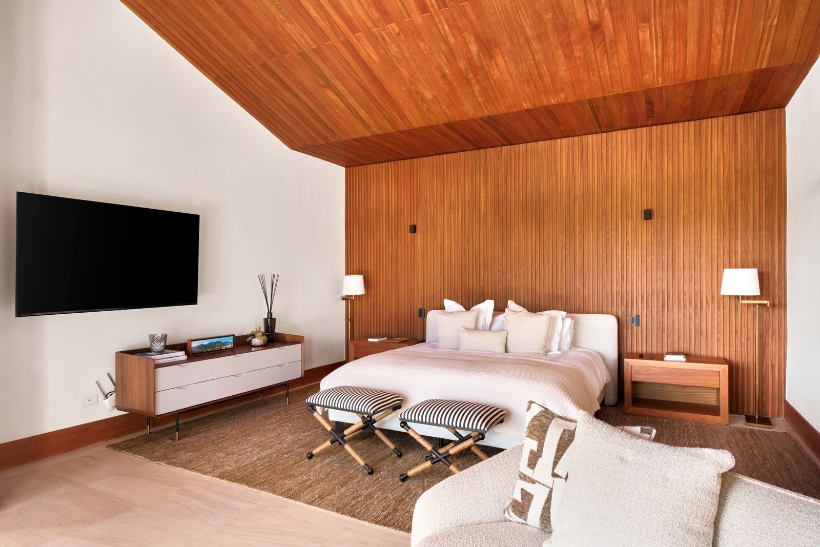 Een moderne slaapkamer met een groot bed, nachtkastjes, een flatscreen televisie en een houten plafond.