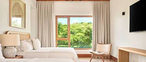 A hotel room with a large bed, a desk, a chair, a TV, and a window with a view of greenery.