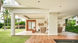 A modern outdoor living area with a wooden deck, a seating area with woven chairs, and a water feature.
