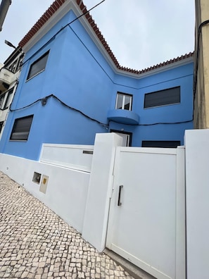 A building with a blue facade, a white gate, and a cobblestone path. - A spacious and comfortable house, just 300 meters from the beach; pets welcome. (Buarcos)