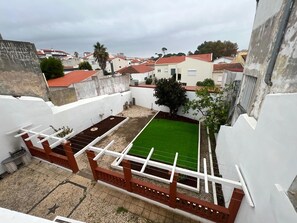 A courtyard with a green artificial turf, a white wall, and a red fence. - A spacious and comfortable house, just 300 meters from the beach; pets welcome. (Buarcos)