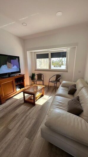 A living room with a leather sofa, a wooden coffee table, a television, and a window with blinds. - A spacious and comfortable house, just 300 meters from the beach; pets welcome. (Buarcos)