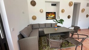 Una sala de estar con un sofá modular, una mesa de comedor con sillas, un cuadro en la pared y varios sombreros colgados.
