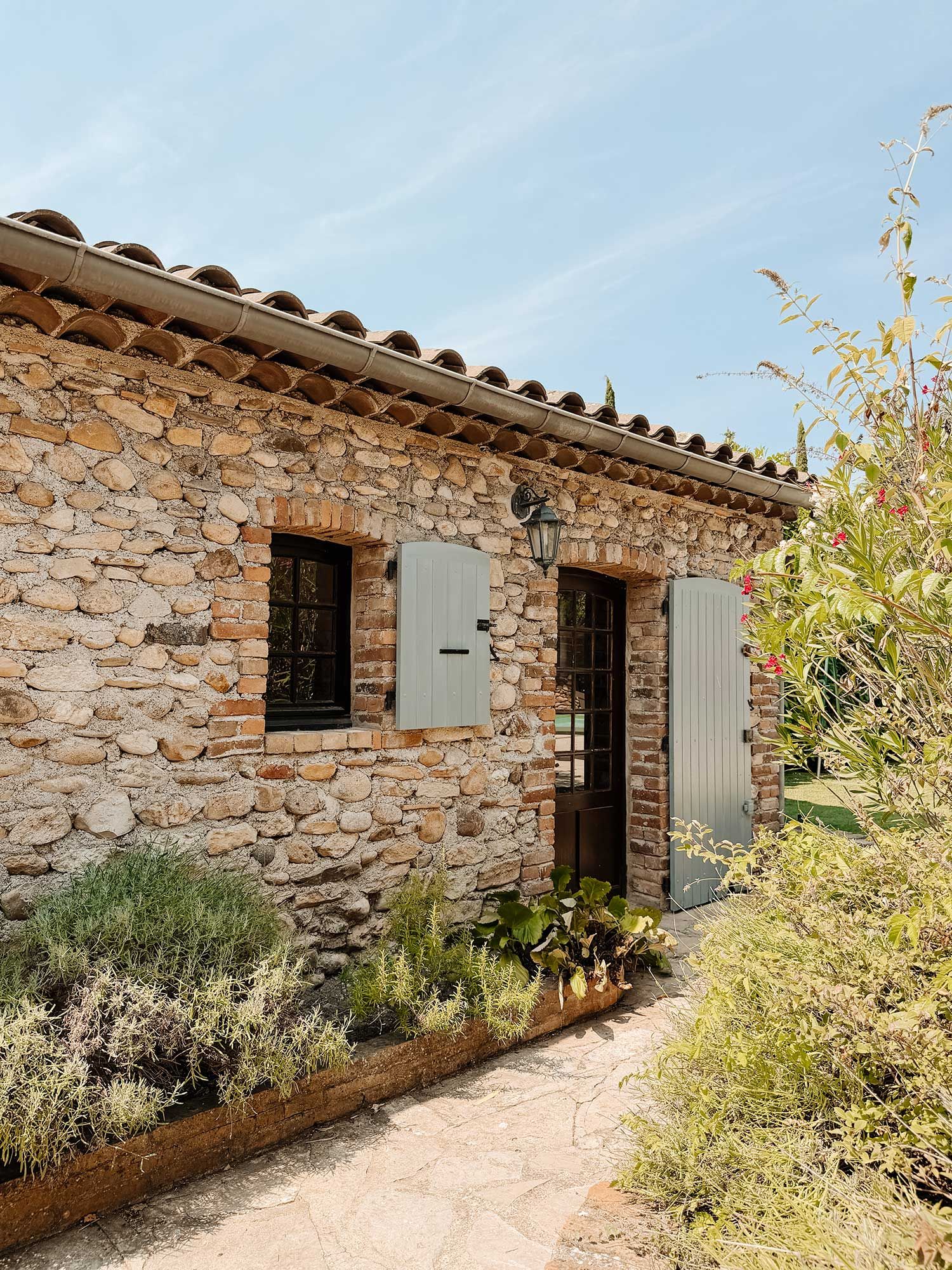 A stone building with a tiled roof, two windows with shutters, and a door.