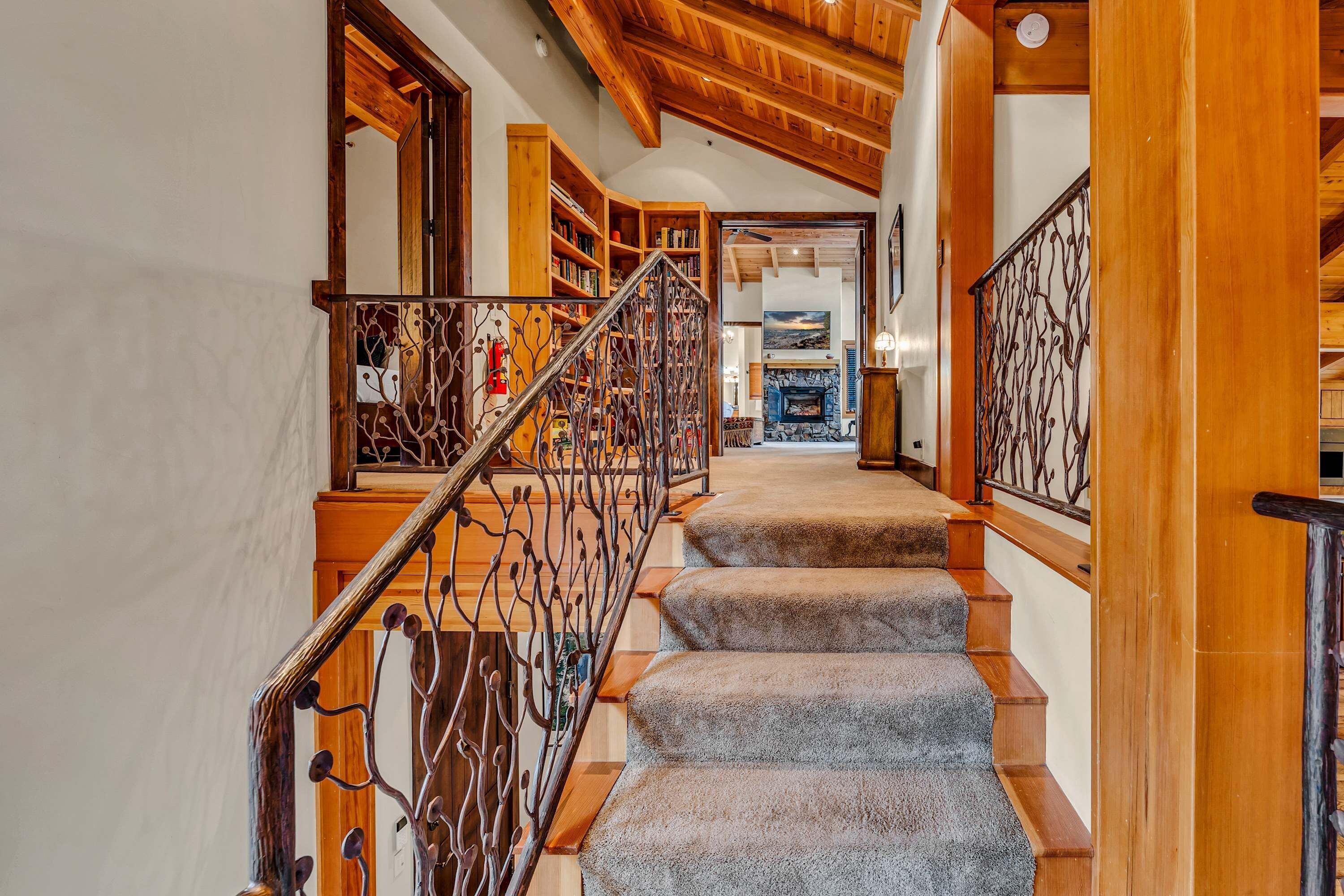 A wooden staircase with a metal railing leading to a living area with a fireplace.