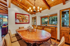 A spacious dining area with a large wooden table, comfortable seating, and a view of the outdoors through large windows. - Lake Tahoe Oasis | Deck & Grill & Hot Tub (Carnelian Bay)