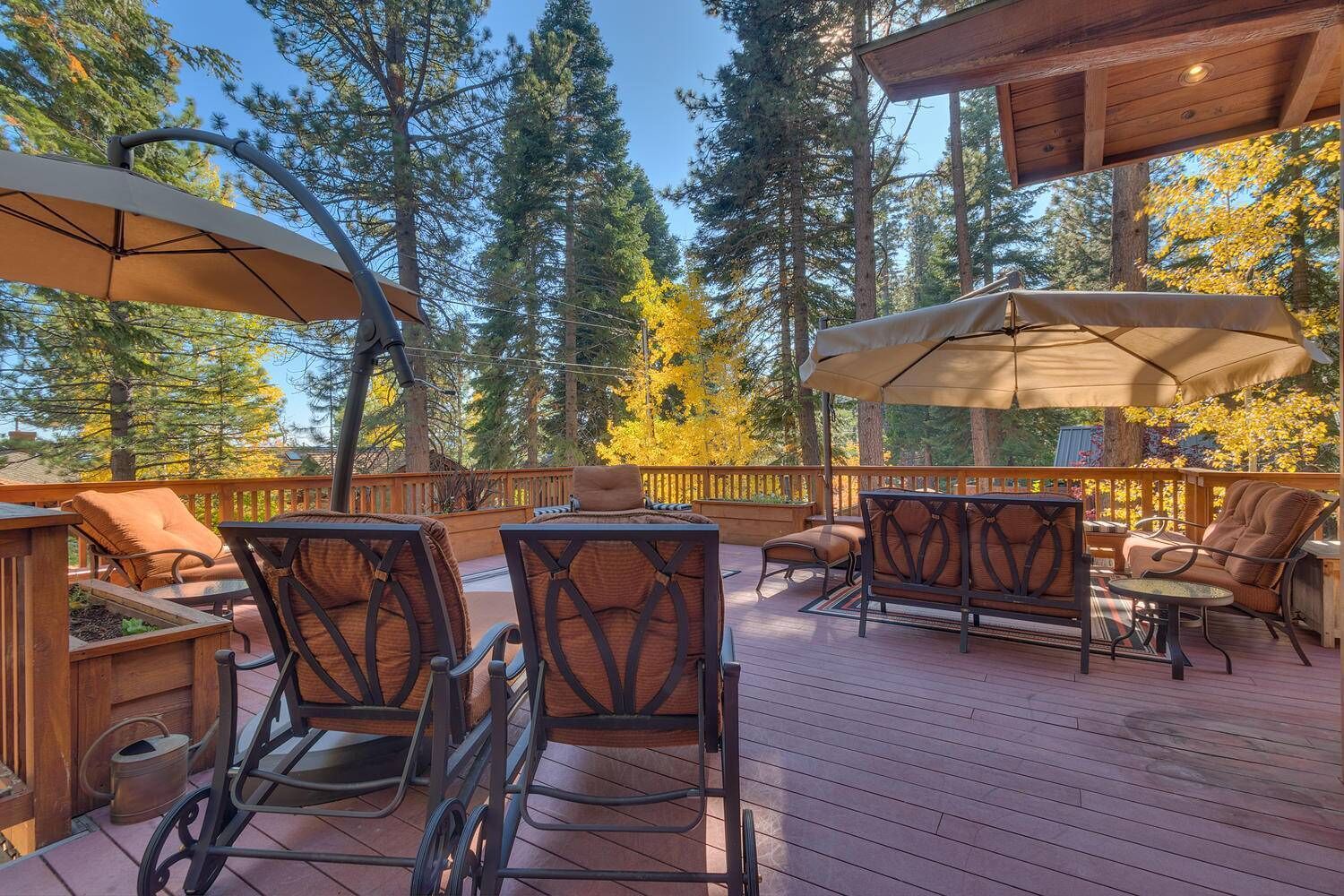 A wooden deck with outdoor furniture, including chairs and a table, surrounded by trees.