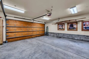 A garage with a wooden door, fluorescent lighting, and a concrete floor. - Lake Tahoe Oasis | Deck & Grill & Hot Tub (Carnelian Bay)