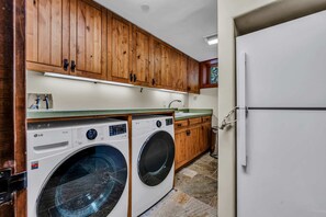 A laundry room with two LG washing machines, wooden cabinets, a sink, and a white refrigerator. - Lake Tahoe Oasis | Deck & Grill & Hot Tub (Carnelian Bay)