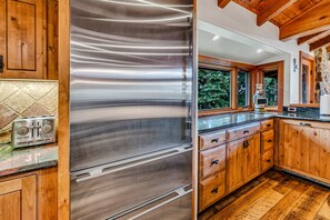 Cozinha moderna com eletrodomésticos de aço inoxidável, armários de madeira e painel de pedra.
