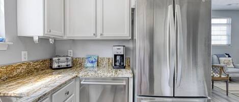 A kitchen with white cabinets, a stainless steel refrigerator, a toaster, and a coffee maker on the countertop.