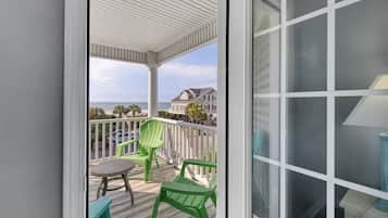 A covered balcony with a view of the ocean, green chairs, and a table.