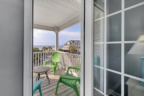 A covered balcony with a view of the ocean, green chairs, and a table.