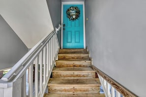 A wooden staircase leading to a turquoise door with a wreath.