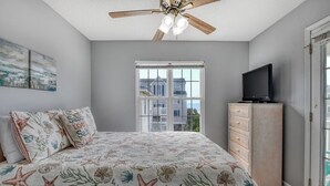 Una camera da letto con un letto, una ventola a soffitto, una televisione su una cassettiera e una finestra vista edifici.