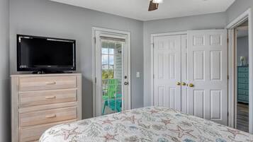 A bedroom with a bed, a television on a dresser, a ceiling fan, and a door leading to a balcony.