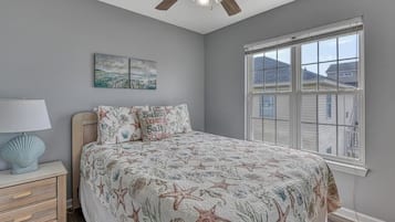 A bedroom with a bed, a nightstand, a lamp, a ceiling fan, a window, and a wall-mounted artwork.