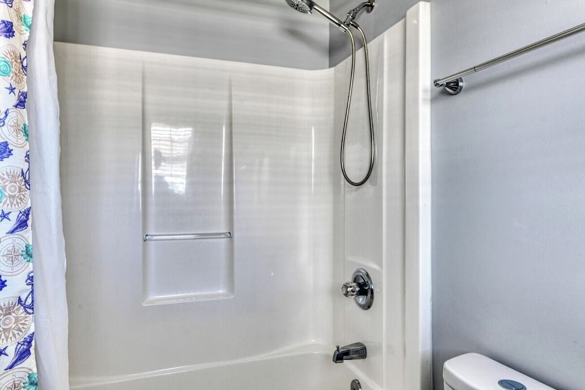 Une salle de bain avec une douche, des toilettes et une fenêtre avec un rideau.